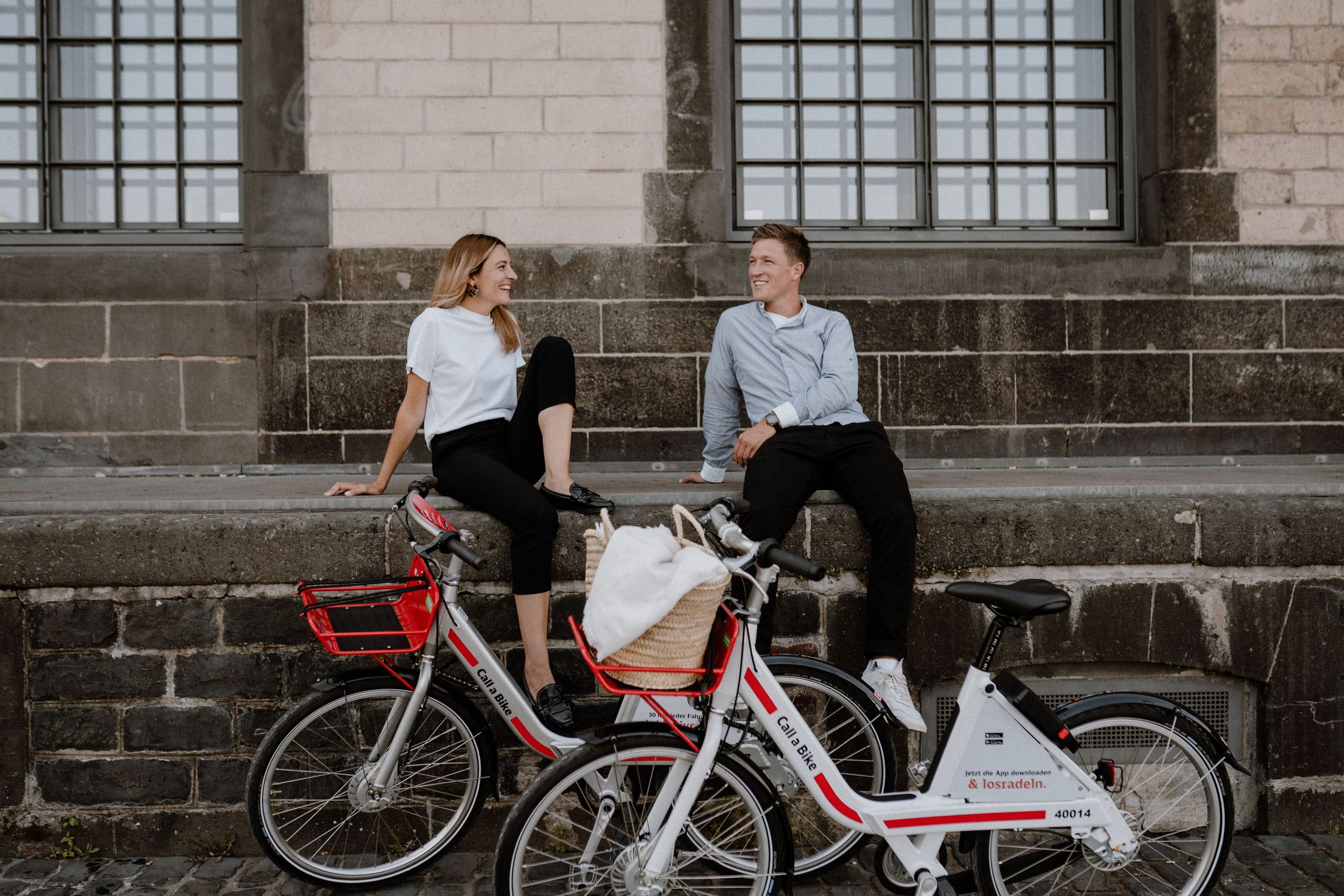 Woman and man sitting in front of building with their Call a Bike bikes