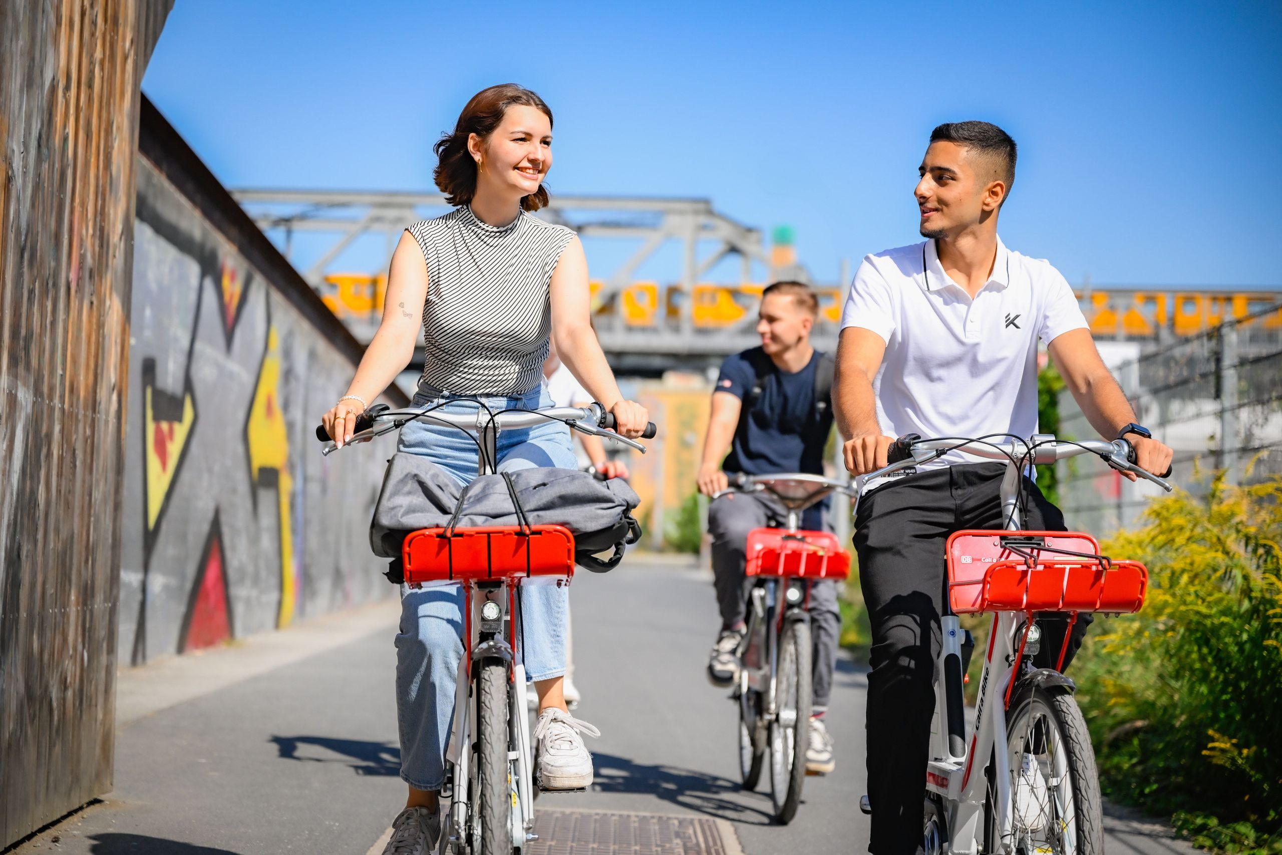 Woman and man riding Call a Bike bicycles through a park